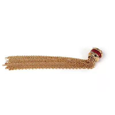 Close-up Exotica Jewel Apliqué Ruby: a decorative appliqué with multiple fine golden metal chains hanging from a golden cylindrical element encrusted with bright red stones.
