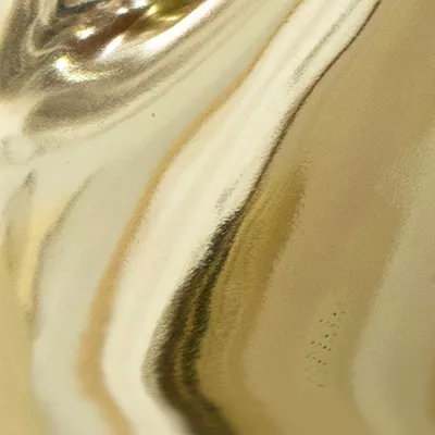 A close-up of a highly reflective gold surface with a smooth, liquid-like appearance, showcasing Koket's Gold Plated Brass (Gloss) finish.
