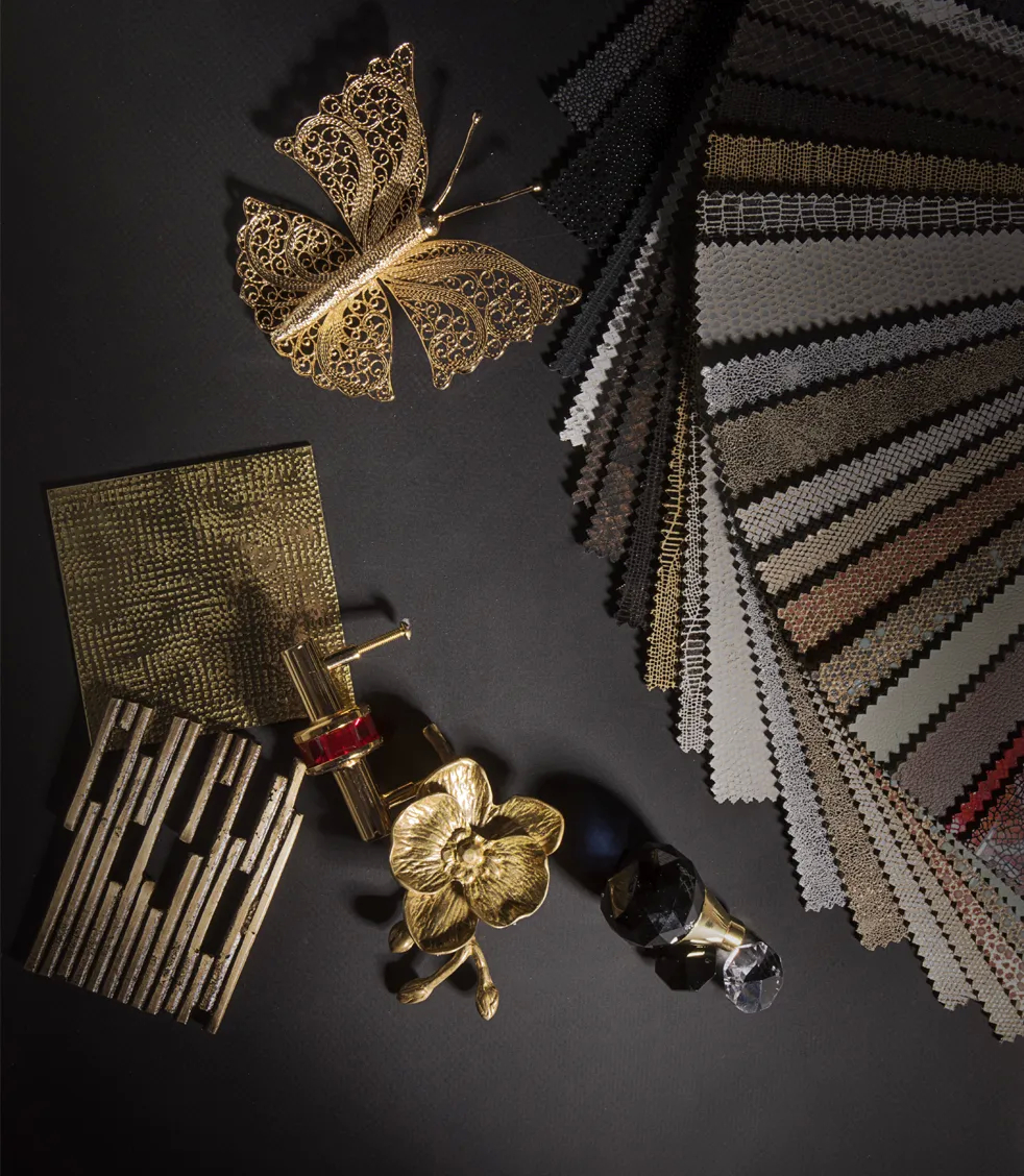 A flat lay showcases luxurious KOKET finishes: metallic fabrics, a gold butterfly, a textured gold square, and a decorative gold flower.
