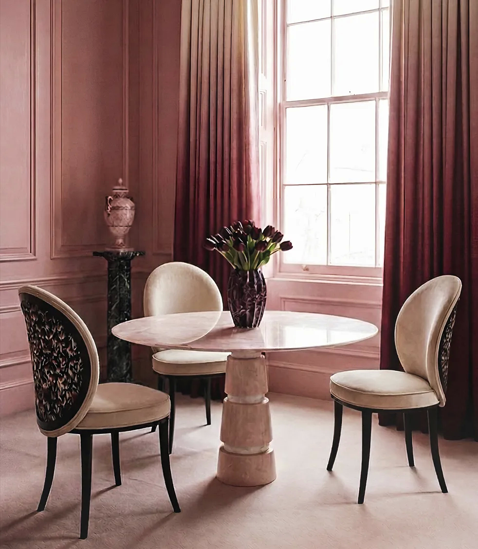 Luxury cinematic dining room with sculptural velvet chairs and round marble pedestal table, framed by blush pink walls and dramatic burgundy curtains, evoking bold femininity and Hollywood Regency-inspired interior design by KOKET.