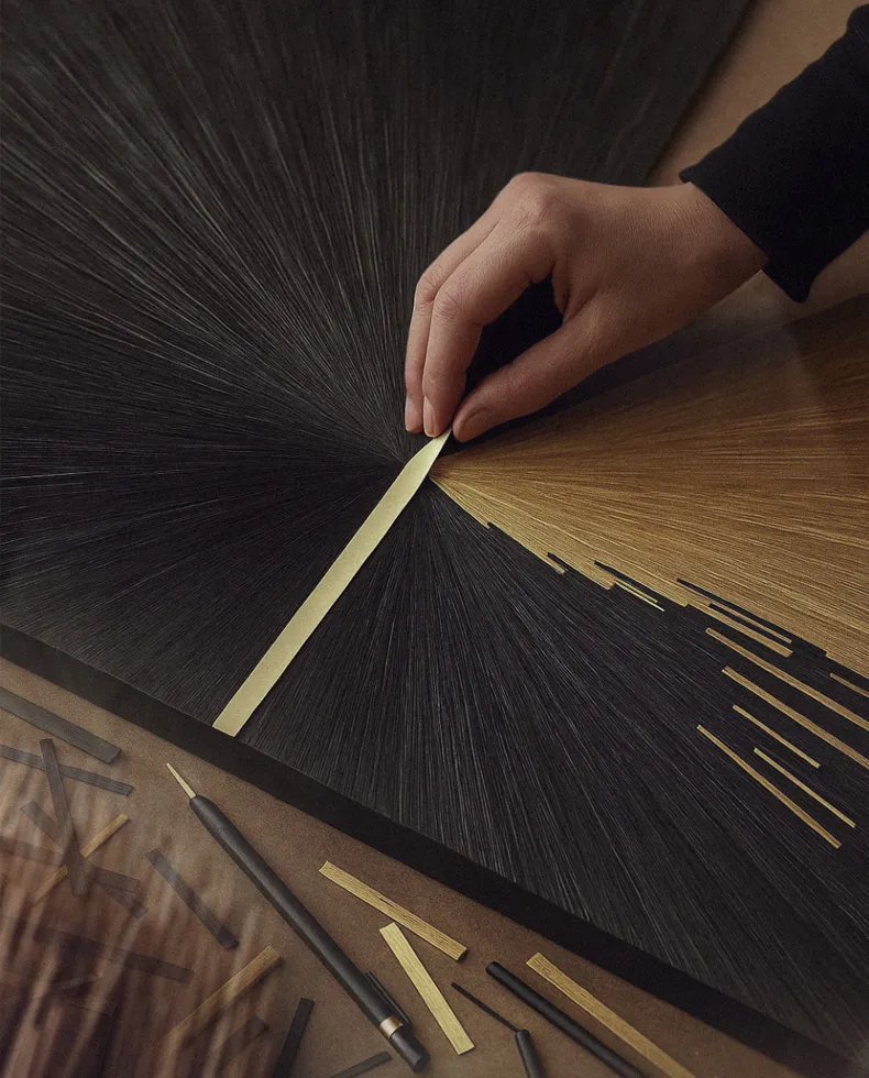 A close-up of hands applying intricate gold and black wood inlay to a luxury furniture piece, showcasing detailed craftsmanship.