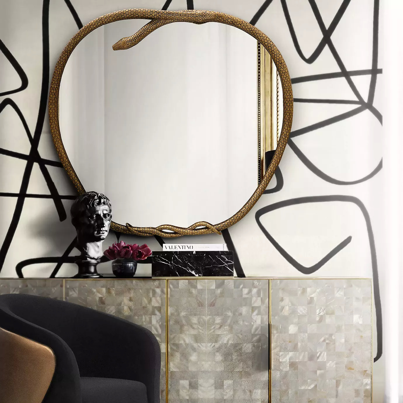 A Serpentine Apple Shaped Mirror, framed by a golden snake, hangs above a marble-topped cabinet in a chic room.