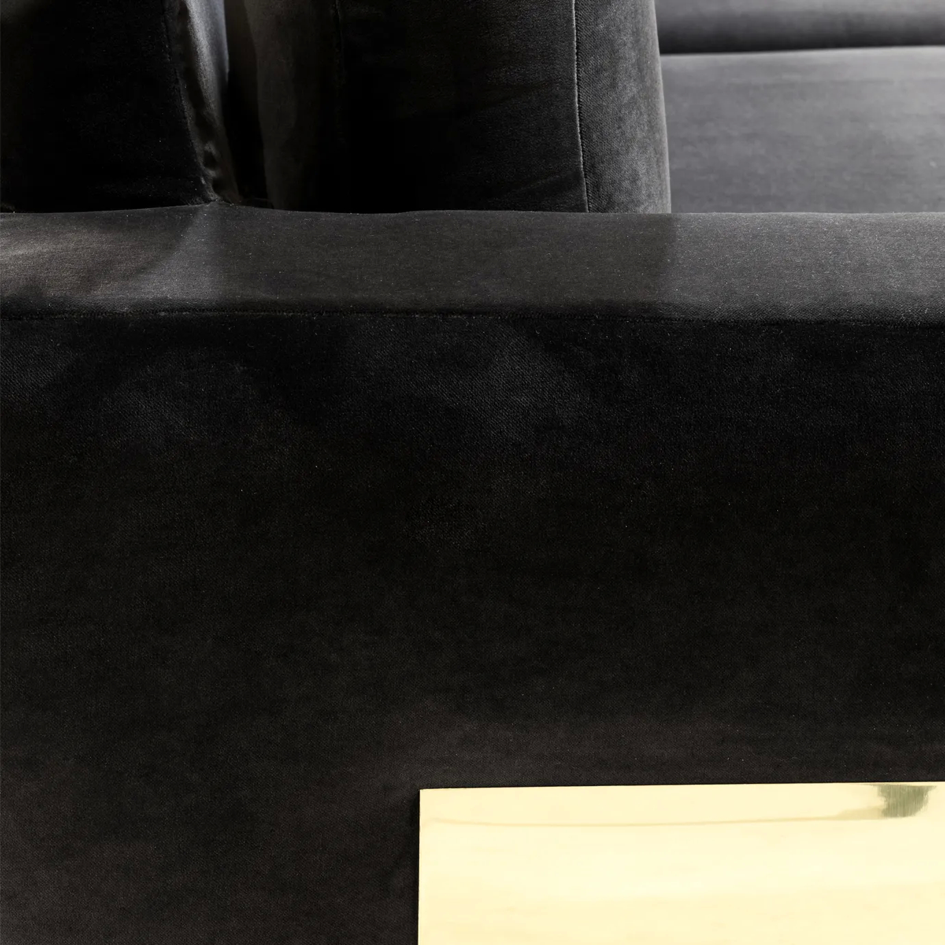 A close-up of the Sofia Sofa highlights the plush black velvet upholstery and the sleek, reflective gold accent on its base.