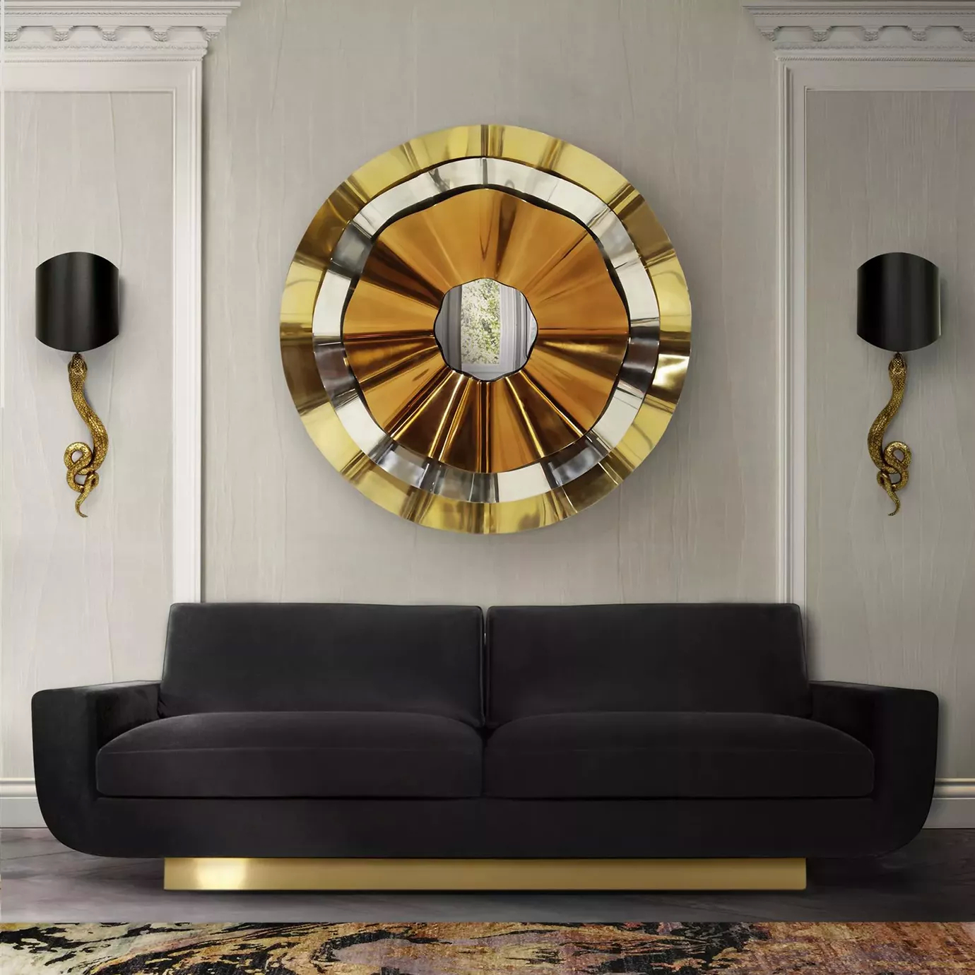 A luxurious Sofia Sofa in black velvet with a gold base sits in a stylish room beneath a large, ornate gold and silver round mirror.