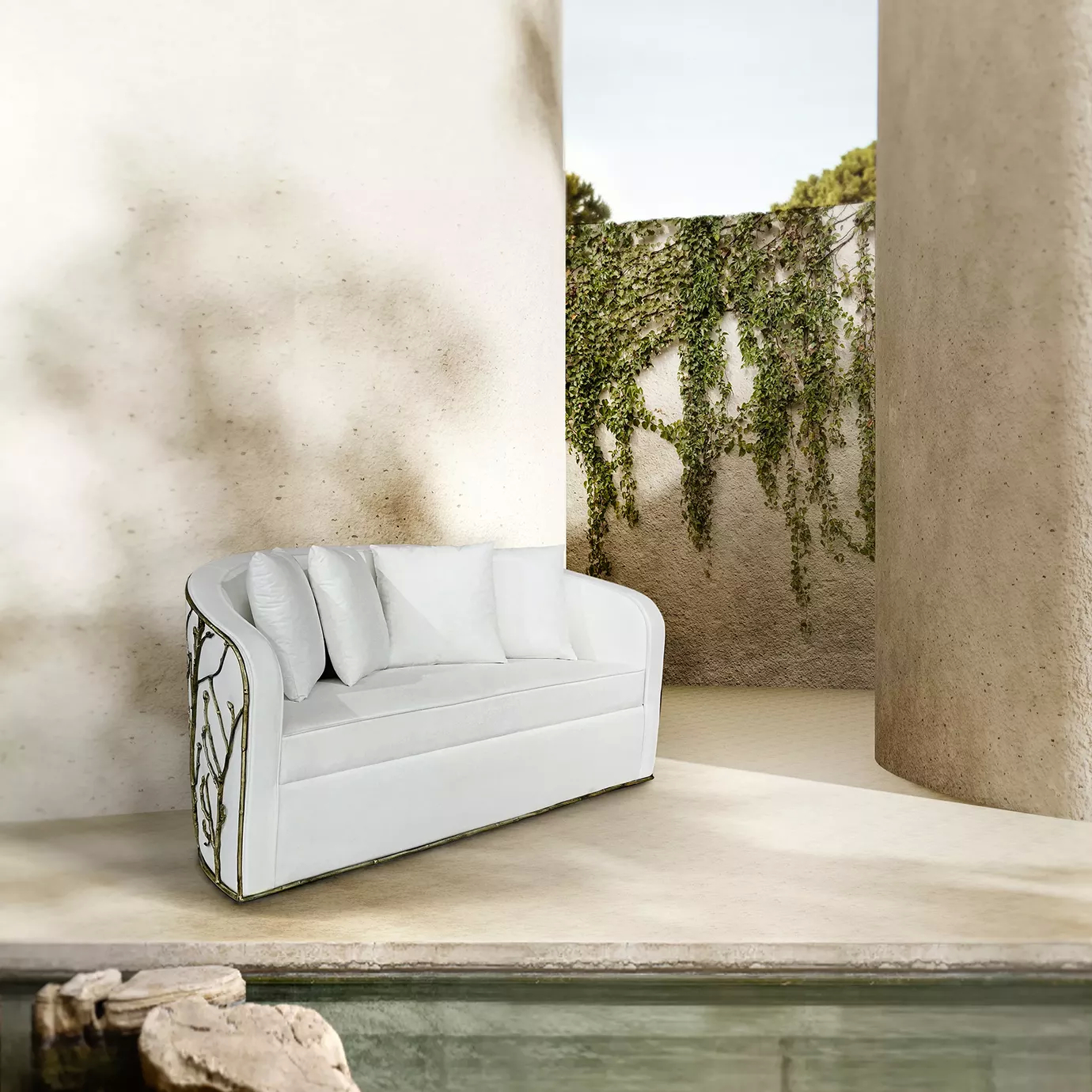 Set by a poolside, an Enchanted Sofa showcases its intricate aged brass structure resembling branches, combining with the elegant white upholstery.