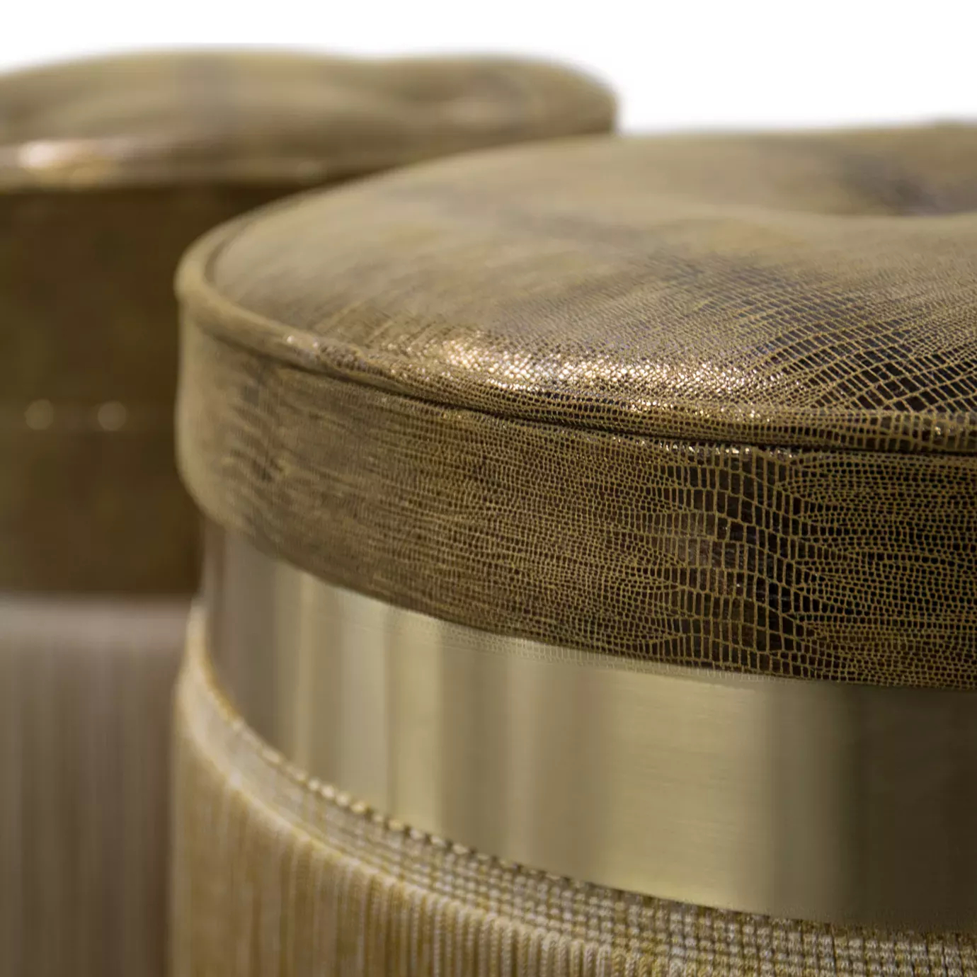 Elegant close-up of two Isabella Stools with textured leather seats in golden tones and cylindrical bases with golden bands and fringes.