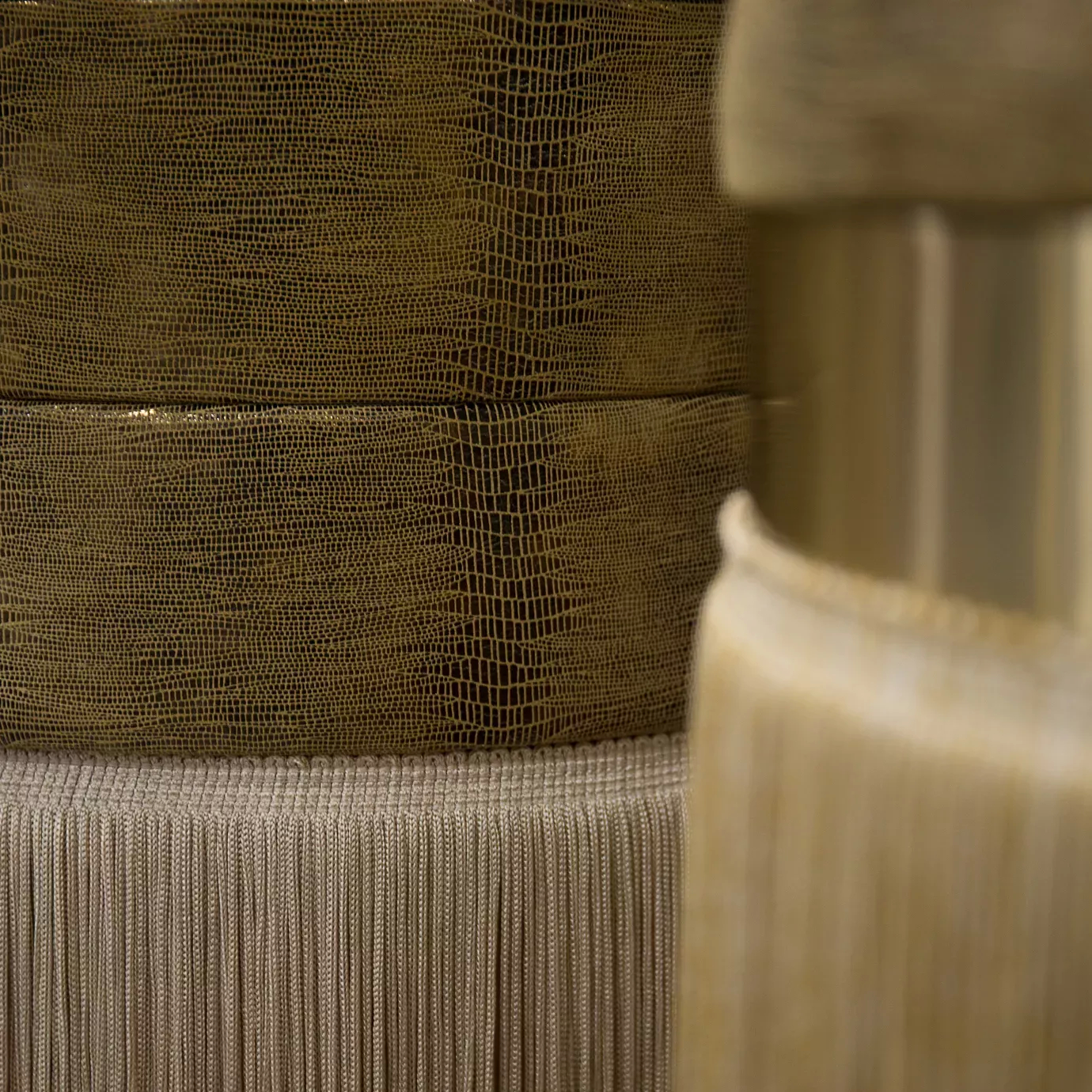 Elegant close-up of two Isabella Stools with textured leather seats in golden tones and cylindrical bases with golden bands and fringes.