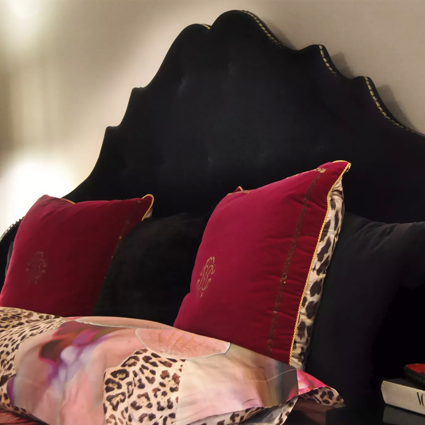 Elegant detail of the black velvet headboard with golden studs of the Alexia Bed with decorative pillows and patterned bedding.
