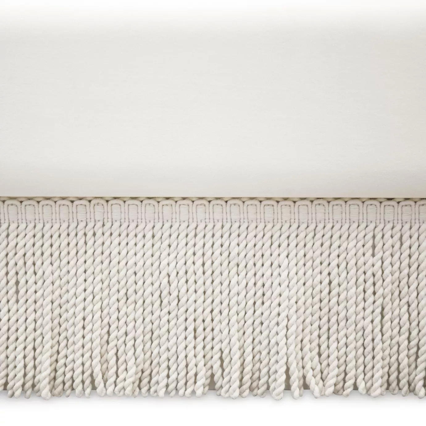 Elegant close-up of the thick light-toned fringes detail of the Sevilliana Bed's base.