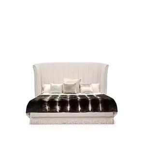 Elegant Sevilliana Bed with high headboard and light textured fabric upholstery with vertical button-tufted details, light bedding, and a dark fur throw with fringes.