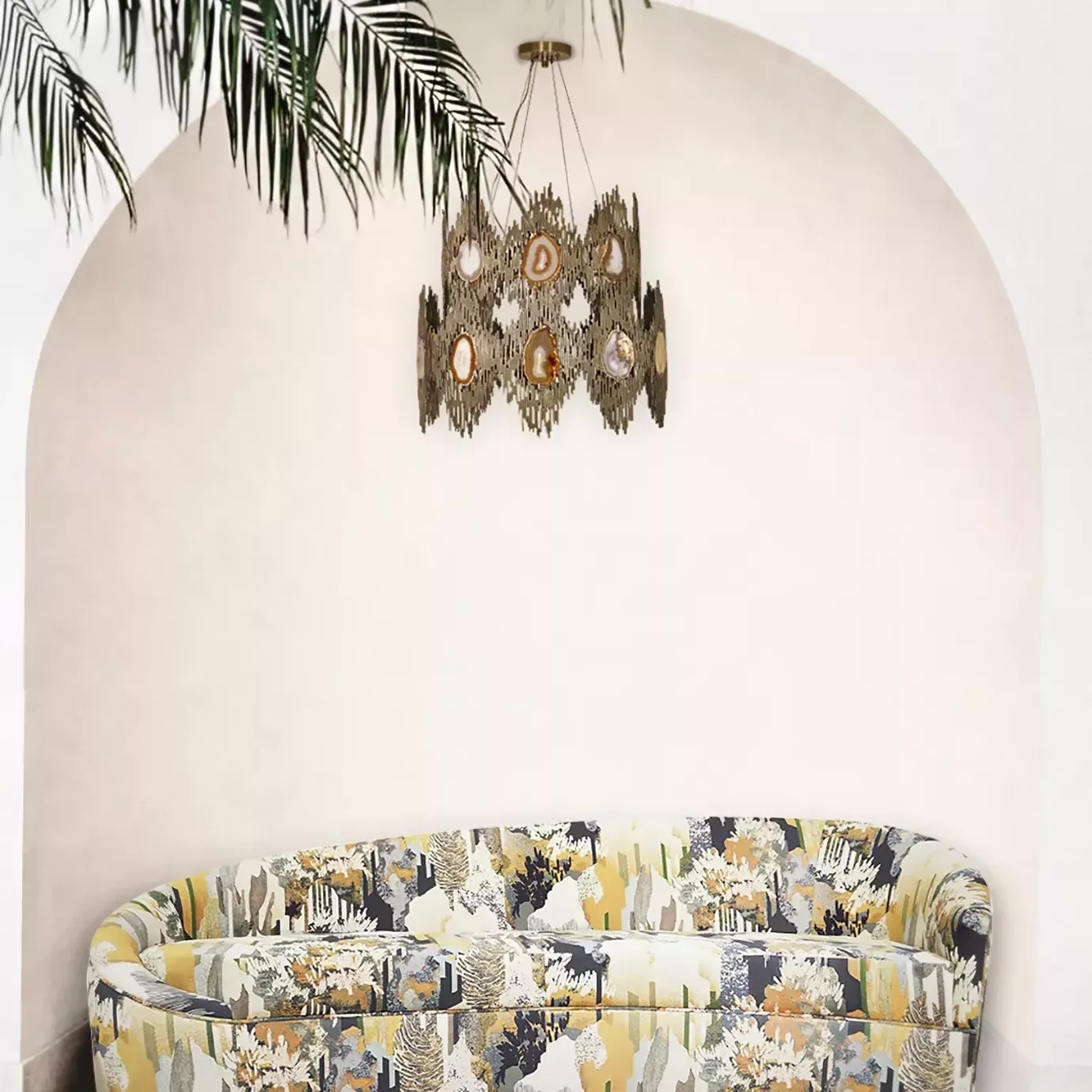 Elegant living room with a curved sofa featuring colorful patterned upholstery under the Vivre 2 Rings Chandelier and next to a plant with large leaves.