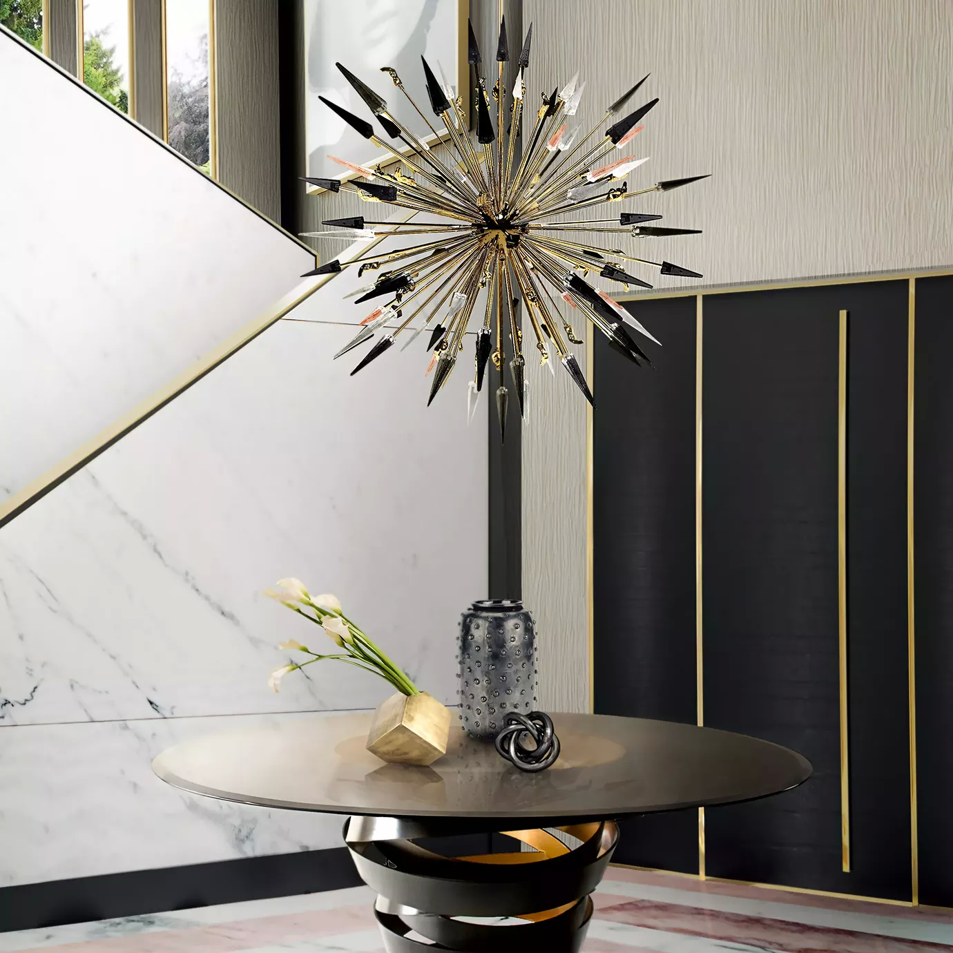 Elegant entryway with a modern round table in dark tones with golden accents and the Outburst Chandelier suspended above, in front of a wall with geometric panels in marble and black with golden details.