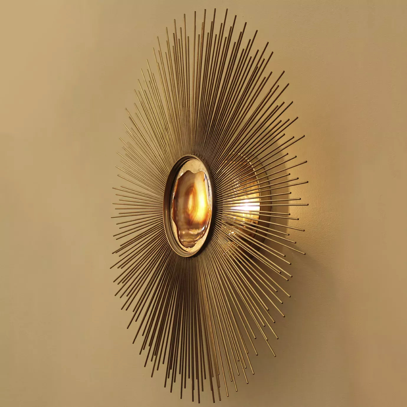Elegant Brilliance Sconce with a sculptural radial design in golden tones mounted on a light wall, featuring an illuminated translucent central detail with shades of white and orange.
