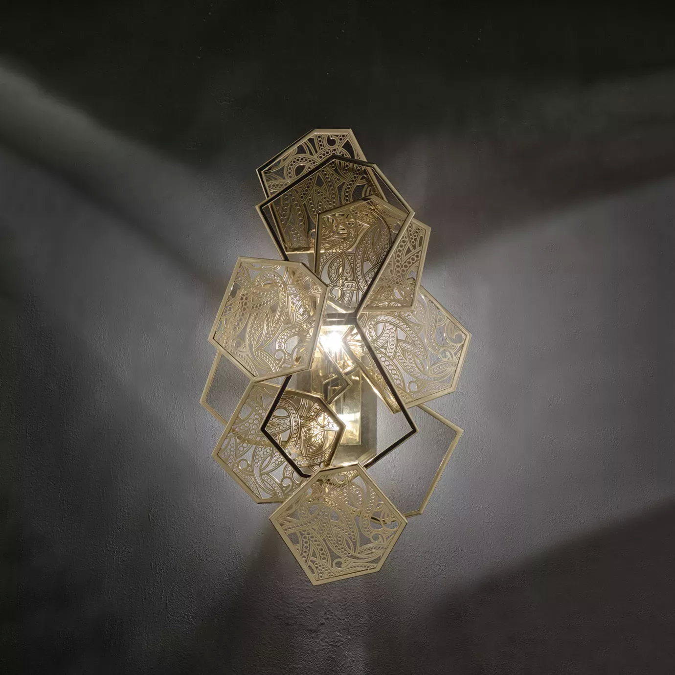 Elegant Hypnotic Sconce with a geometric design in golden tones and bronze glass details featuring intricate patterns, mounted on a dark wall and emitting a soft light.