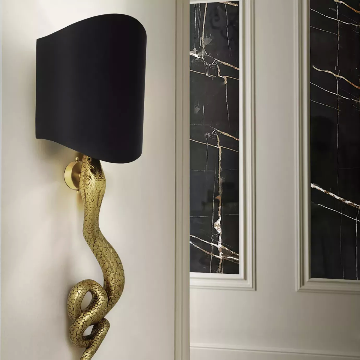 Elegant detail of a sculptural golden Serpentine Sconce with a black lampshade, mounted on a light wall next to a door with black marble panels featuring golden veins.