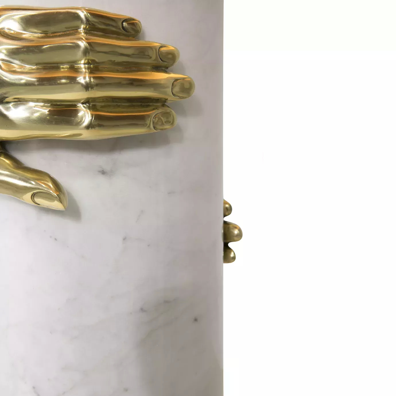 Elegant close-up of the sculptural detail of two golden hands gripping the white marble cylindrical base of the Vengeance Table Lamp.