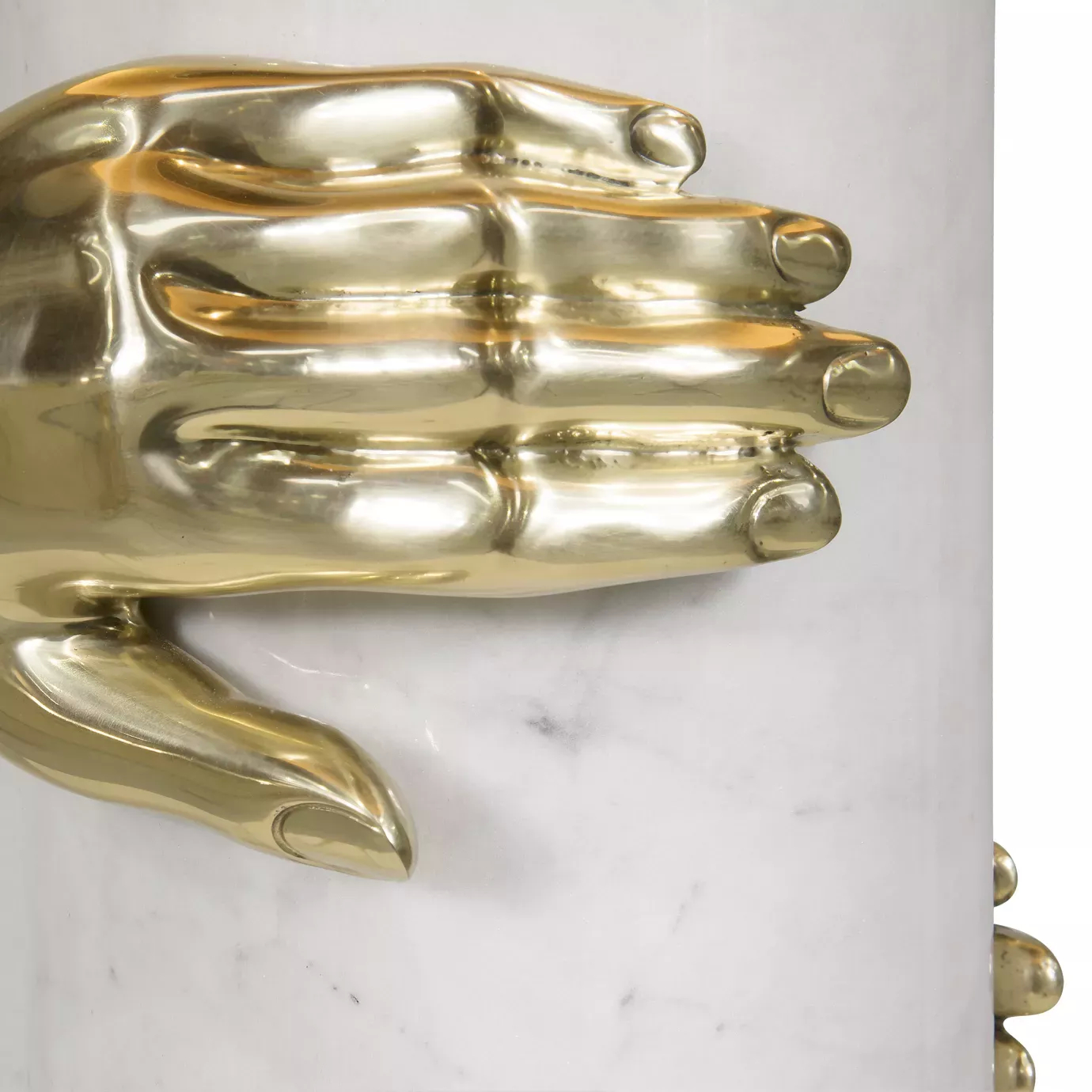 Elegant close-up of the sculptural detail of a polished golden hand gripping the white marble cylindrical base of the Vengeance Table Lamp.