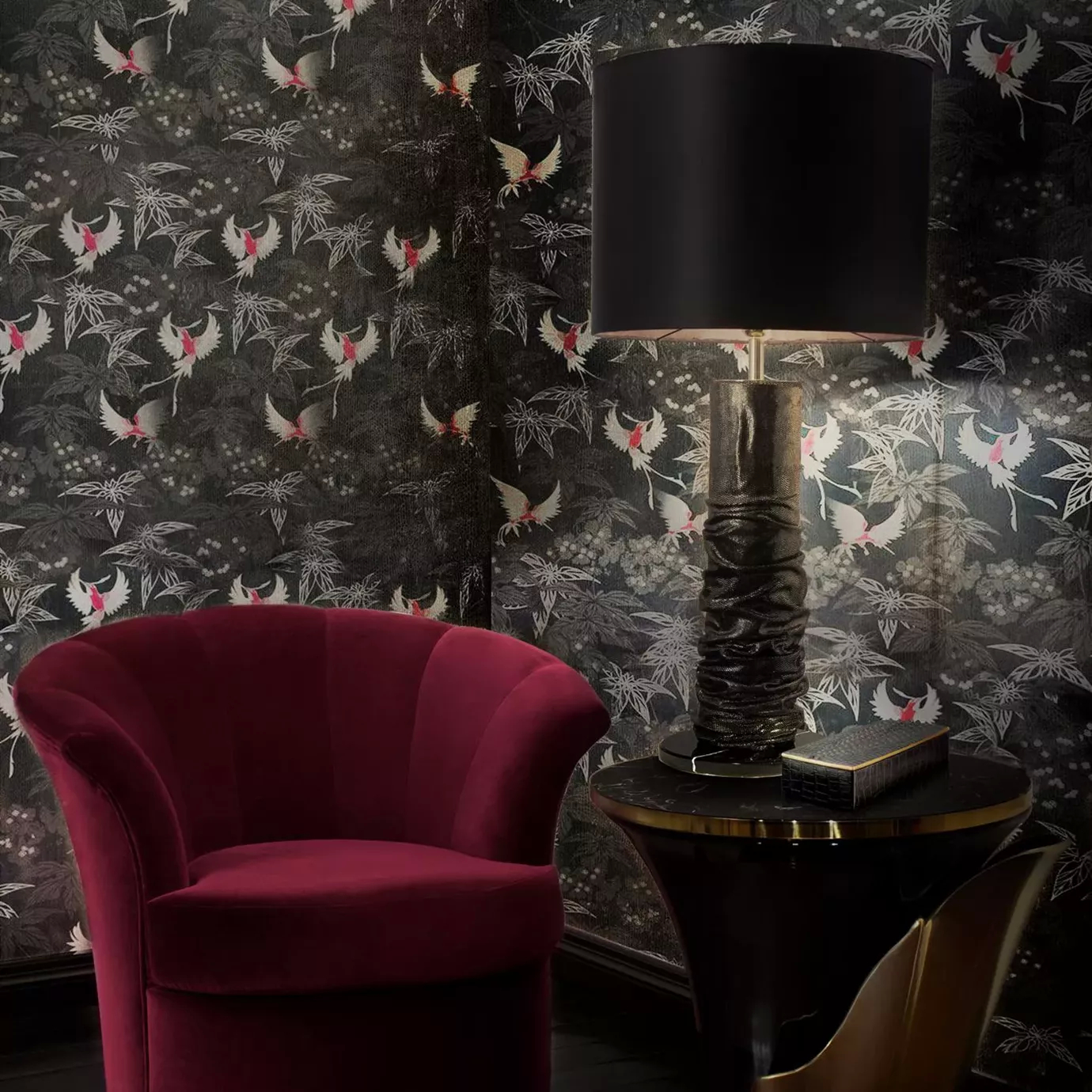 Elegant corner with a armchair upholstered in red velvet, a Ruchê Table Lamp with a textured brown and gold-toned base and a black lampshade on a round black side table with golden details, against a wall with dark-toned bird and foliage patterned wallpaper.
