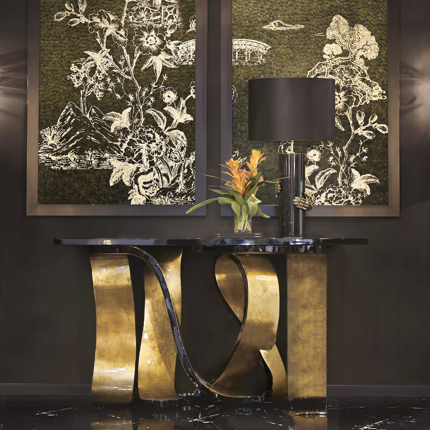An entryway with a luxurious Ribbon Broken Gold Leaf Console, with a distinctive golden base, characterized by its twists and turns, and a black tabletop. On top of the console, there is a black table lamp and a bouquet. Hanging on the wall, there are two paintings in olive hues.