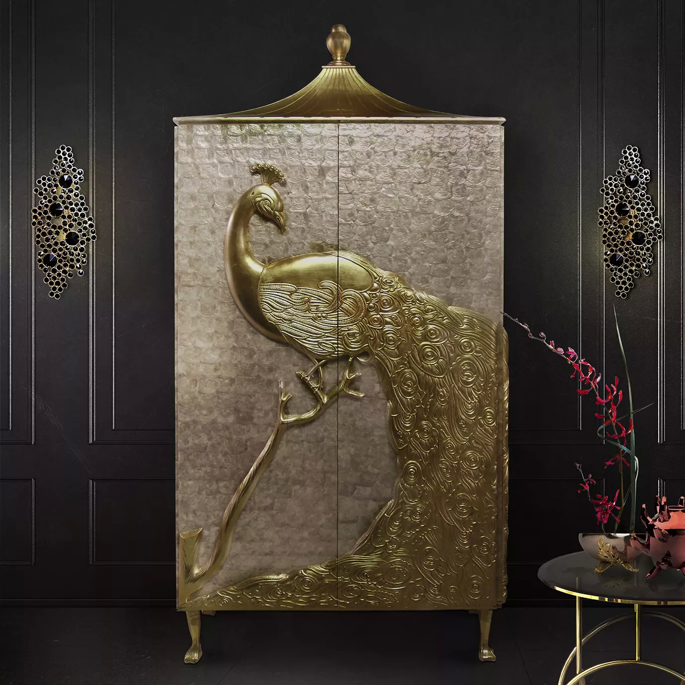 Elegant Camilia Armoire with two doors adorned with a detailed golden sculpture of a peacock against a light-toned textured background, topped with a golden pagoda-shaped roof, in front of a textured black wall with two black and gold Eternity Sconces, and next to a round black side table with golden details and a floral arrangement.