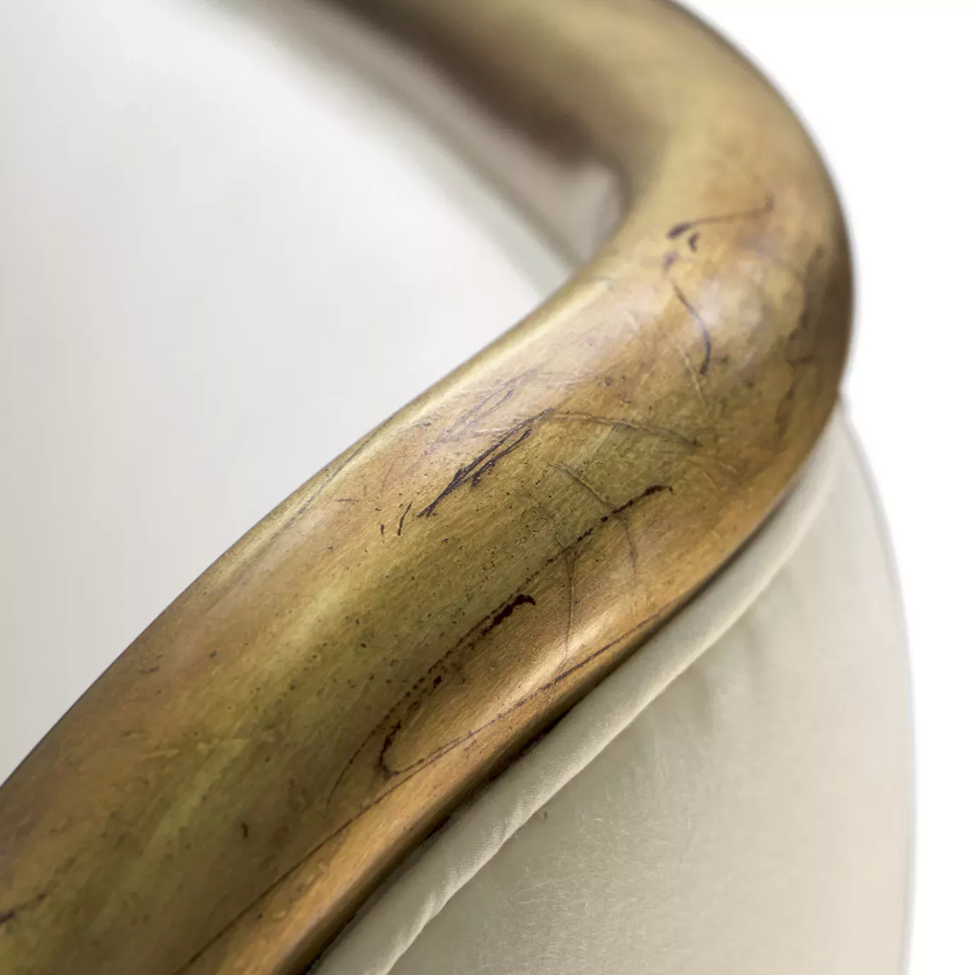 Elegant close-up of the curved golden trim detail of the white fabric upholstered headboard of the Forbidden Plain Bed.