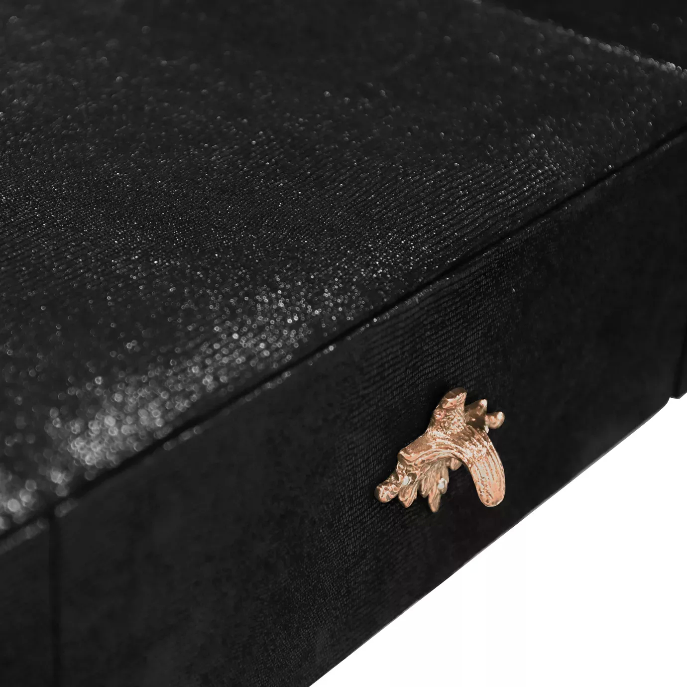 Elegant close-up detail of a decorative copper-toned handle with a floral or star-like design on a black drawer of the Luridae Console.