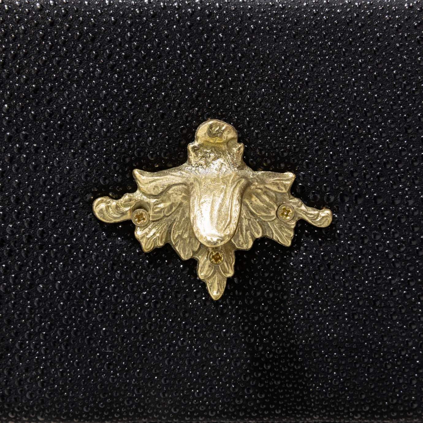 Elegant close-up detail of a decorative golden star-shaped handle on a textured black drawer of the Temptation Console.