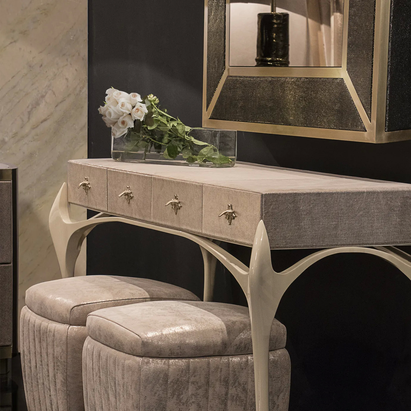 Elegant vanity corner featuring the beige Temptation Console adorned with golden star-shaped handles, topped with a vase of white roses and a rectangular mirror with a textured frame and golden accents, accompanied by two Poufs with beige textured upholstery and sculptural white bases.