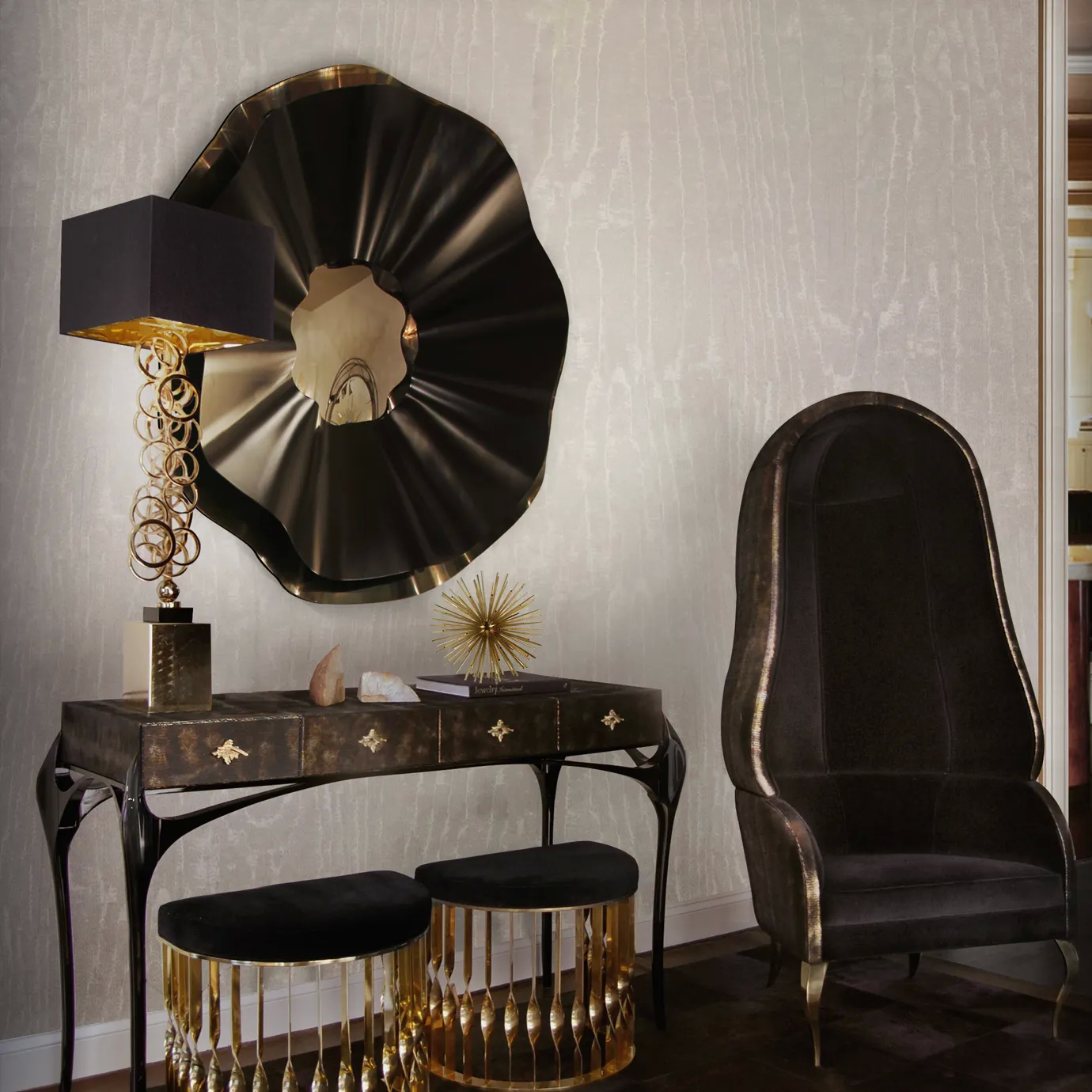 Elegant living room corner with the dark Luridae Console adorned with copper-toned decorative handles, topped with a Table Lamp featuring a textured black base and a black lampshade with golden interior details, and several decorative objects, beneath an Revê Mirror with a black frame and golden accents, flanked by two black Ottomans with golden details and fringes, and a high-backed armchair in dark fabric with golden accents, against a wall with beige-toned textured wallpaper.