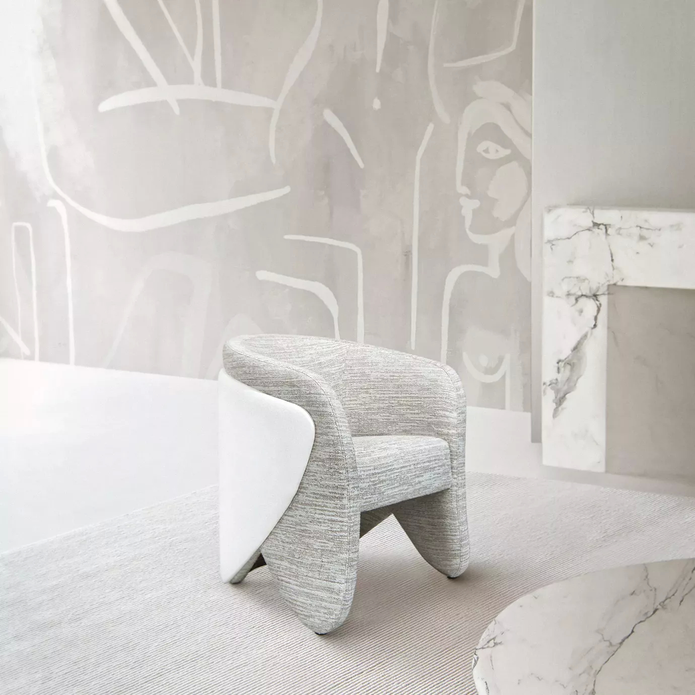 Elegant Denise Chair with a curved design and light grey textured fabric upholstery contrasted by a glossy white side panel, in a minimalist setting with a light rug, a white marble coffee table, and a wall featuring light-toned abstract art and a decorative white marble fireplace.