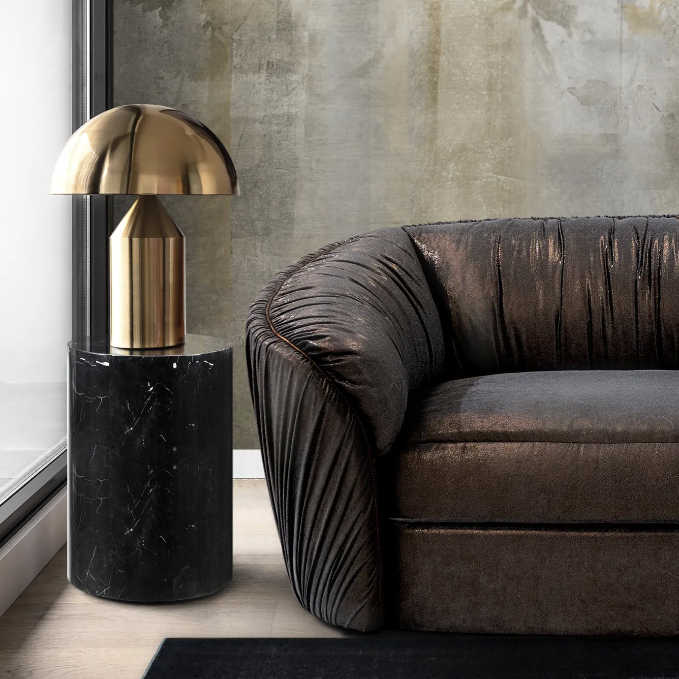 Elegant living room corner featuring part of the Luscious Sofa in pleated brown fabric, next to a cylindrical black marble side table with a golden metal table lamp featuring a dome-shaped shade, on a light wooden floor and a black rug, against a textured wall in neutral tones.