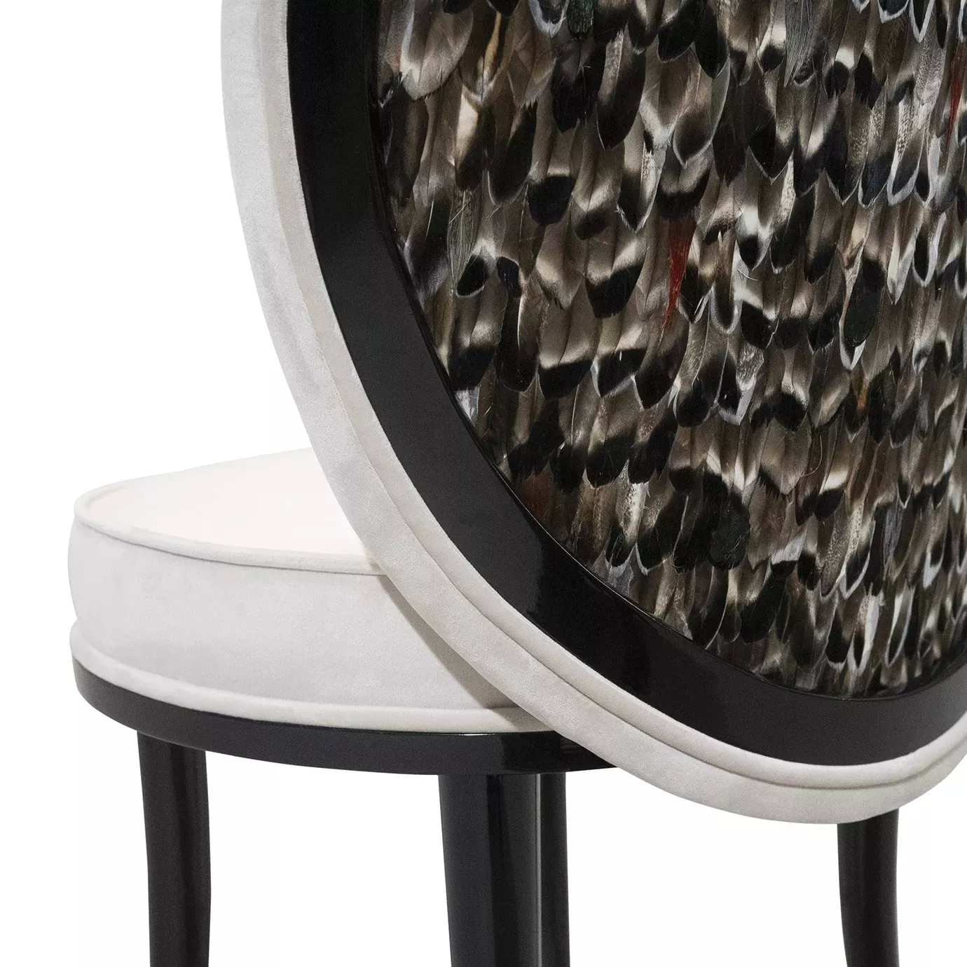 Elegant close-up detail of the curved backrest of the Merveille Folie Dining Chair, adorned with an intricate pattern of feathers in shades of brown, black, and white, framed by white upholstery and a glossy black trim.