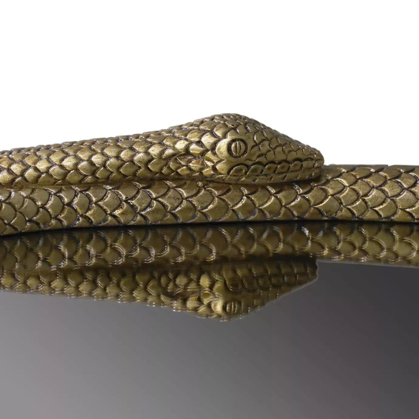 Elegant close-up detail of the golden textured serpent's head with a stylized eye that forms part of the frame of the Serpentine Apple Shaped Mirror, reflected on the mirror's surface.