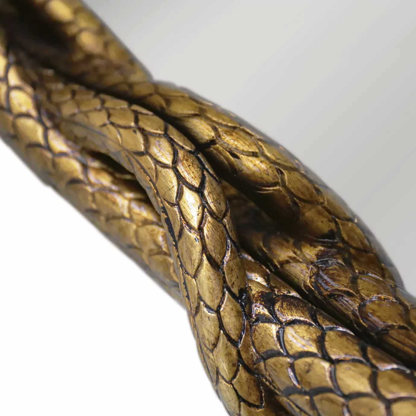 Elegant close-up detail of the golden scaled texture of the intertwined tail of the serpent that forms the base of the Serpentine Apple Shaped Mirror's frame