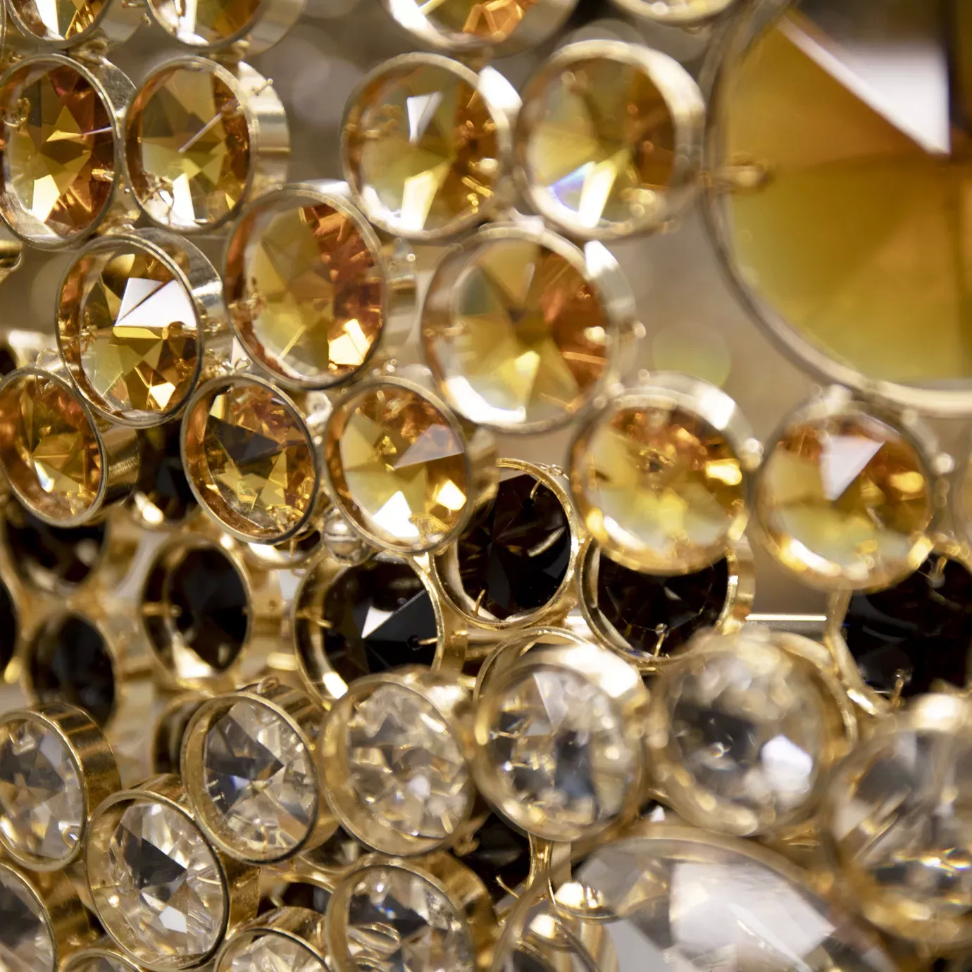 Elegant close-up detail of the faceted golden, black, and clear crystals that adorn the undulating rings of the Trinity Chandelier, capturing the light and revealing their multiple facets.