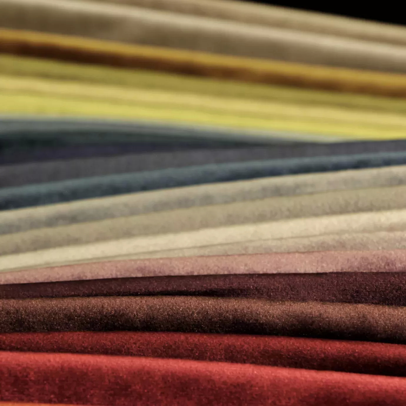Elegant presentation of a wide range of Silky Velvet fabric swatches in diverse rich and luminous tones, arranged in layers, showcasing the smooth texture and silky sheen of the collection from a perspective focused on the variety of colors.