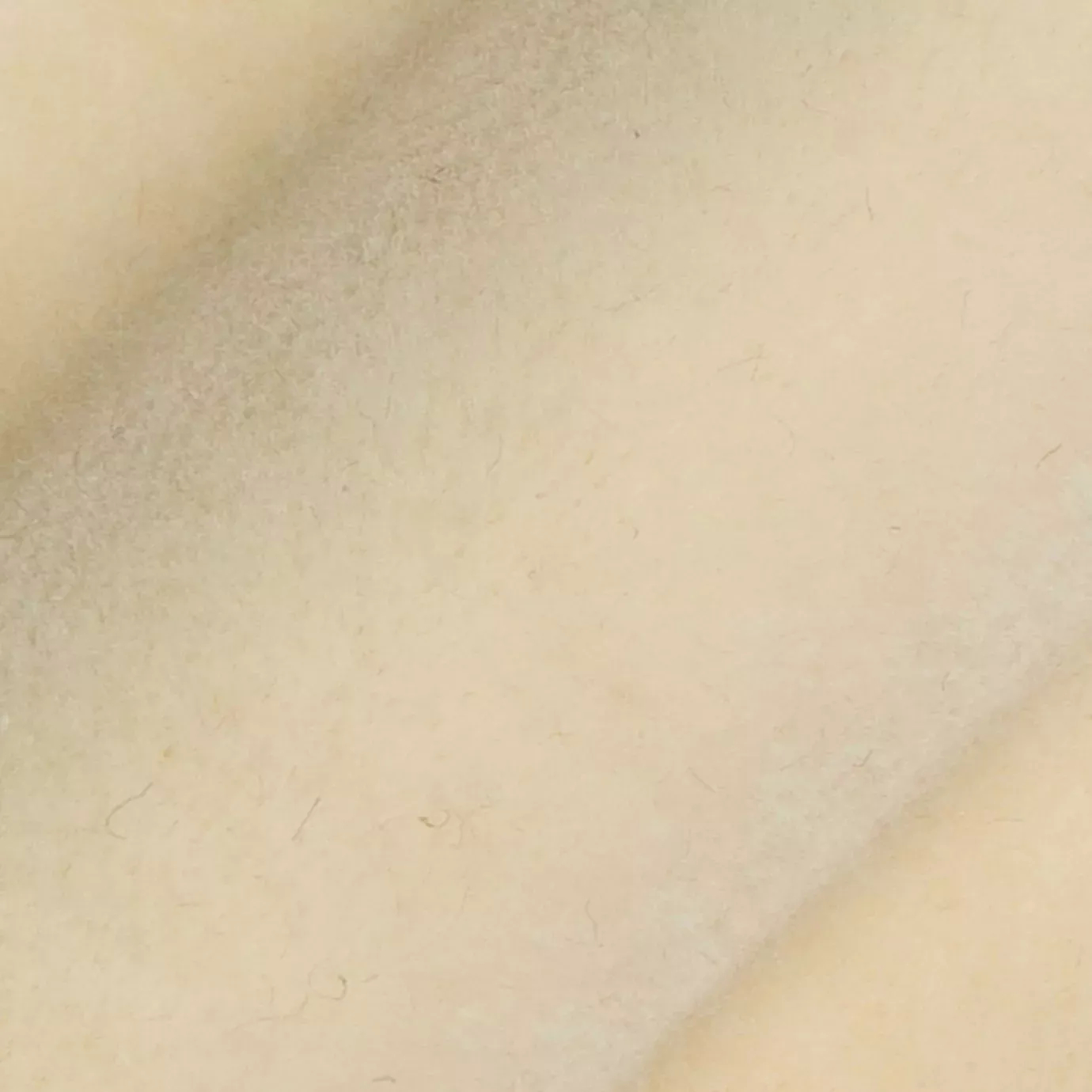 Soft and elegant close-up of a Lux Velvet fabric swatch in a light and luminous cream tone, showcasing its velvety texture and a delicate sheen that gives it a feeling of comfort and gentle elegance.