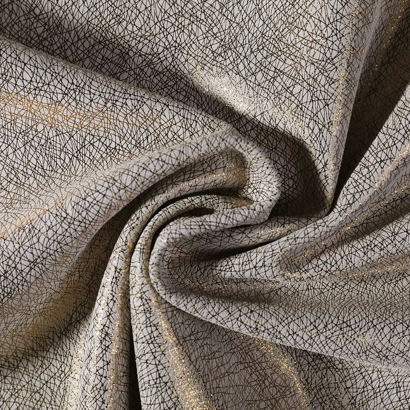 Close-up of a Glamour Leather fabric swatch with an abstract pattern of fine gold and black lines interwoven on a light base, showcasing its unique texture and a subtle sheen that gives it a feeling of modernity and sophistication. The fabric is slightly draped, revealing its pliability and the interplay of light on the different folds.
