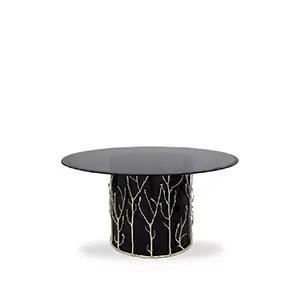 Featuring a smoked glass tabletop, the Enchanted Glass Top Dining Table has a black structure adorned with intricate aged brass details, resembling branches.
