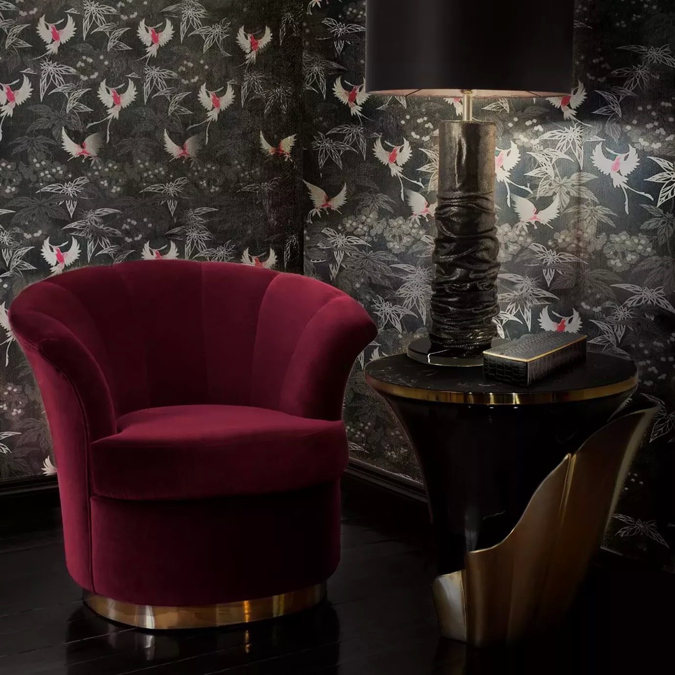 A modern living room corner with and elegant Yasmine Aged Gold Leaf Side Table, featuring an ebony tabletop set on a black wooden base adorned with an aged gold leaf structure. Next to the side table, there’s a pink armchair with a gold metal base. In the background there’s a patterned wallcovering.