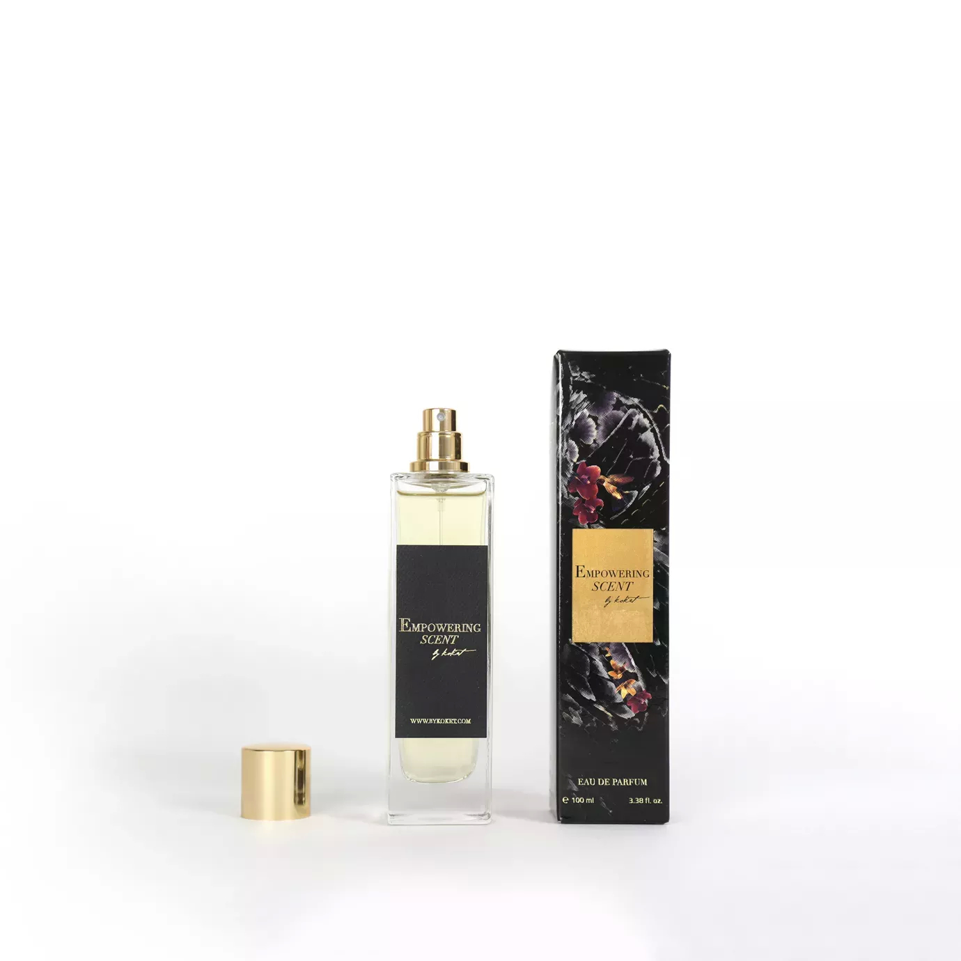 Clear glass Empowering Scent perfume bottle with a gold cap and a black label, next to its dark floral packaging.