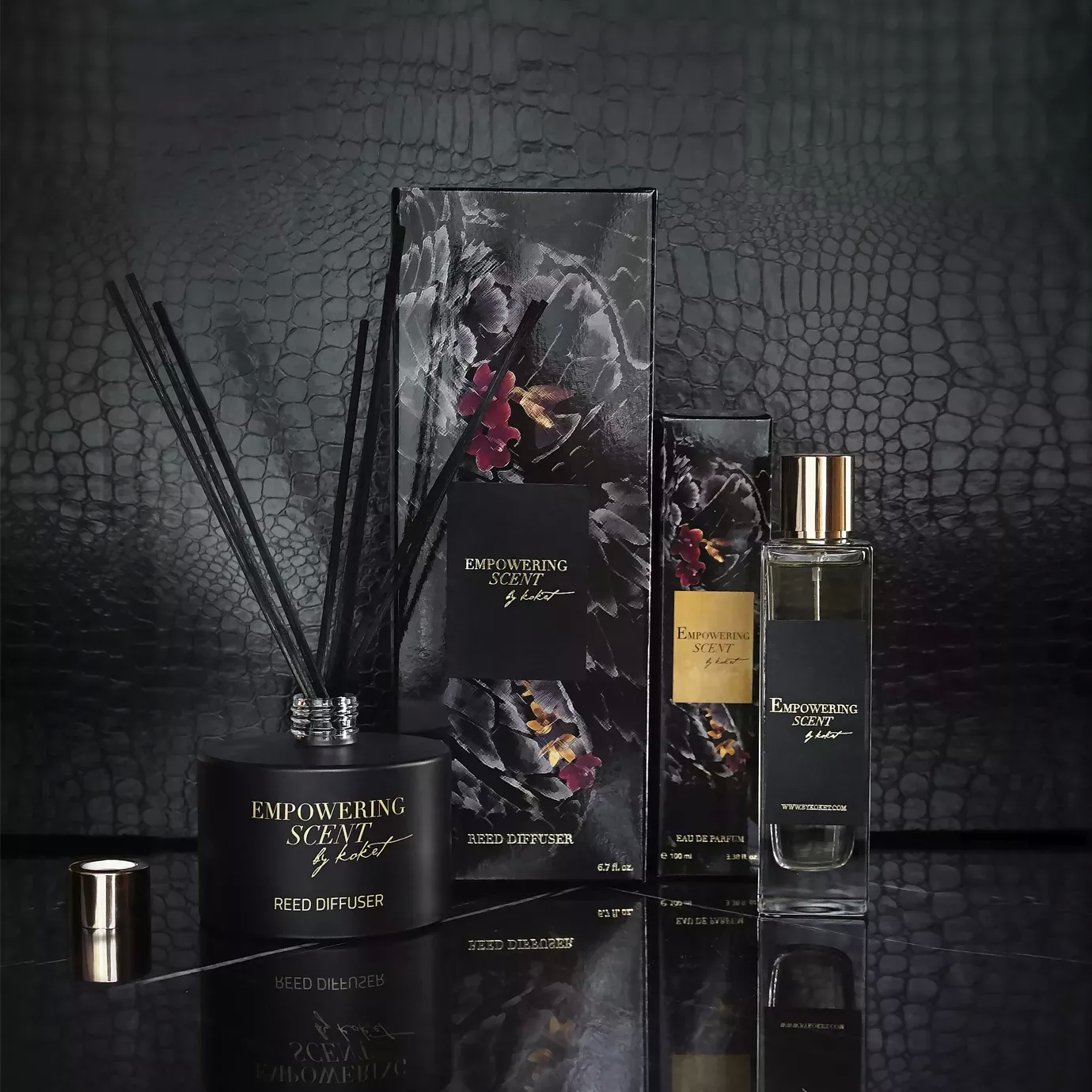 Empowering Scent set: black reed diffuser and matching perfume bottle with gold accents, next to their floral-patterned packaging.