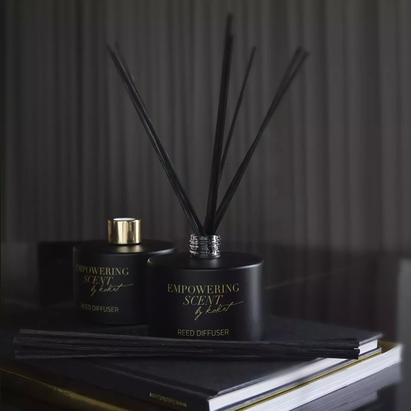 Two black Empowering Diffuser bottles with gold accents and reeds, displayed on a stack of books.