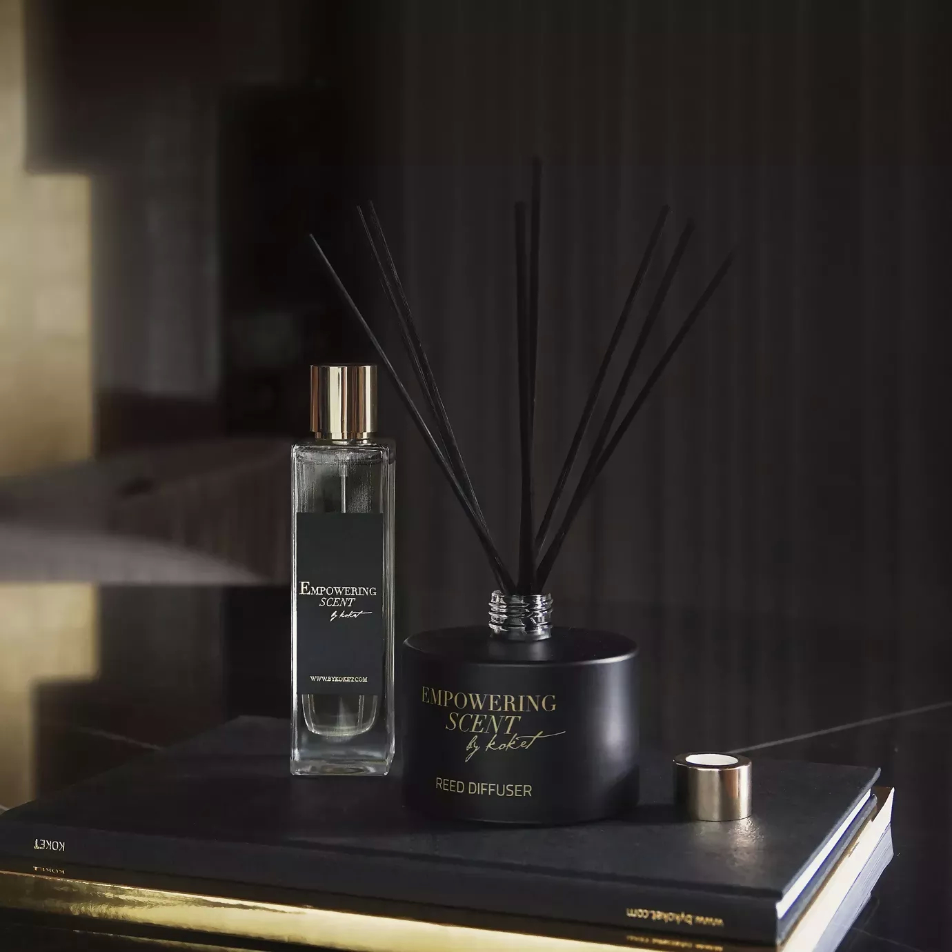 Empowering Diffuser set: black reed diffuser with gold accents and black reeds, alongside a matching perfume bottle, on a book.