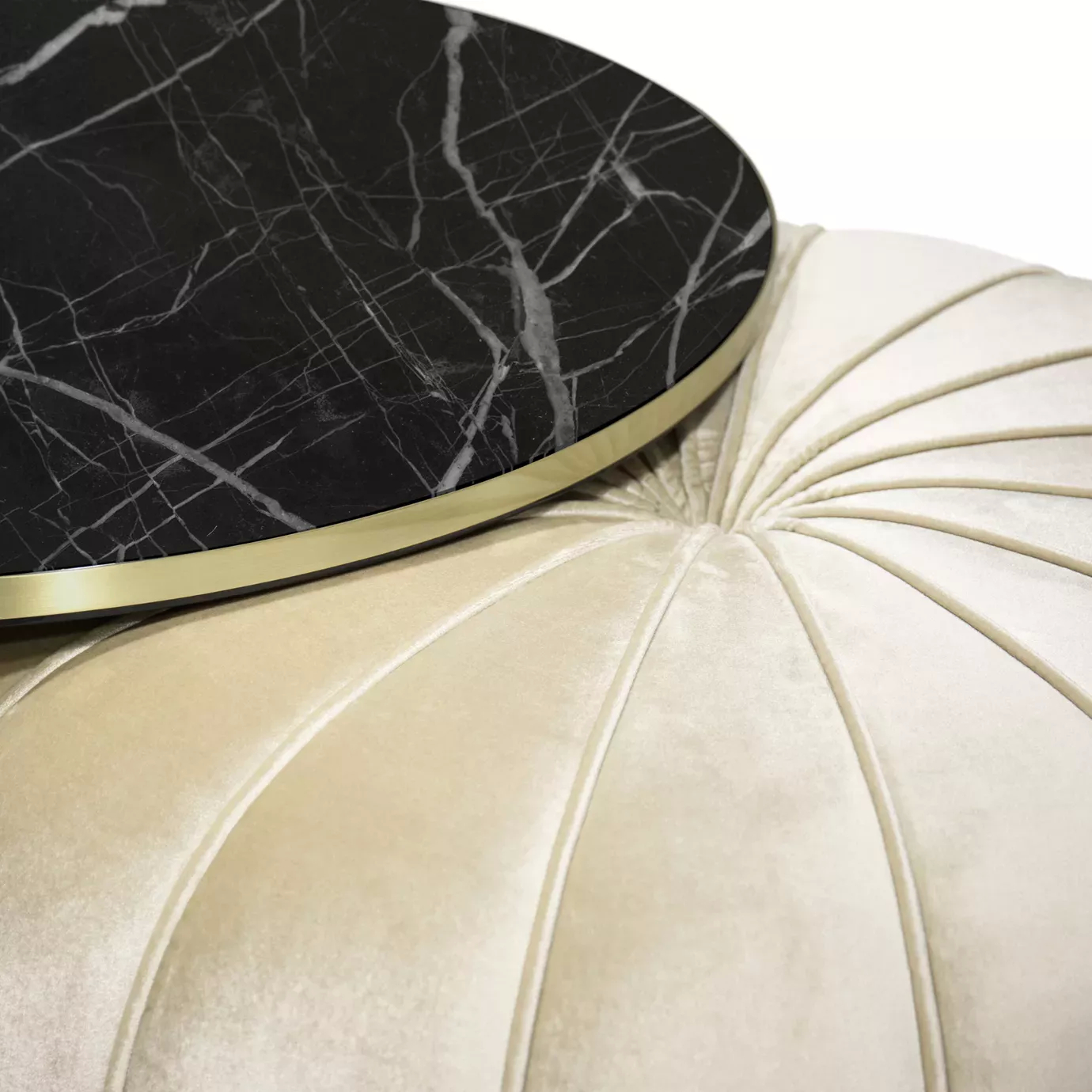 Close-up of the Embrace Coffee Table: Black Nero Marquina marble top with gold trim resting on a plush cream velvet ottoman.
