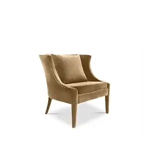 Slightly angled view of the Athina Chair, a wingback armchair upholstered in a soft, golden-brown velvet with a matching square pillow.