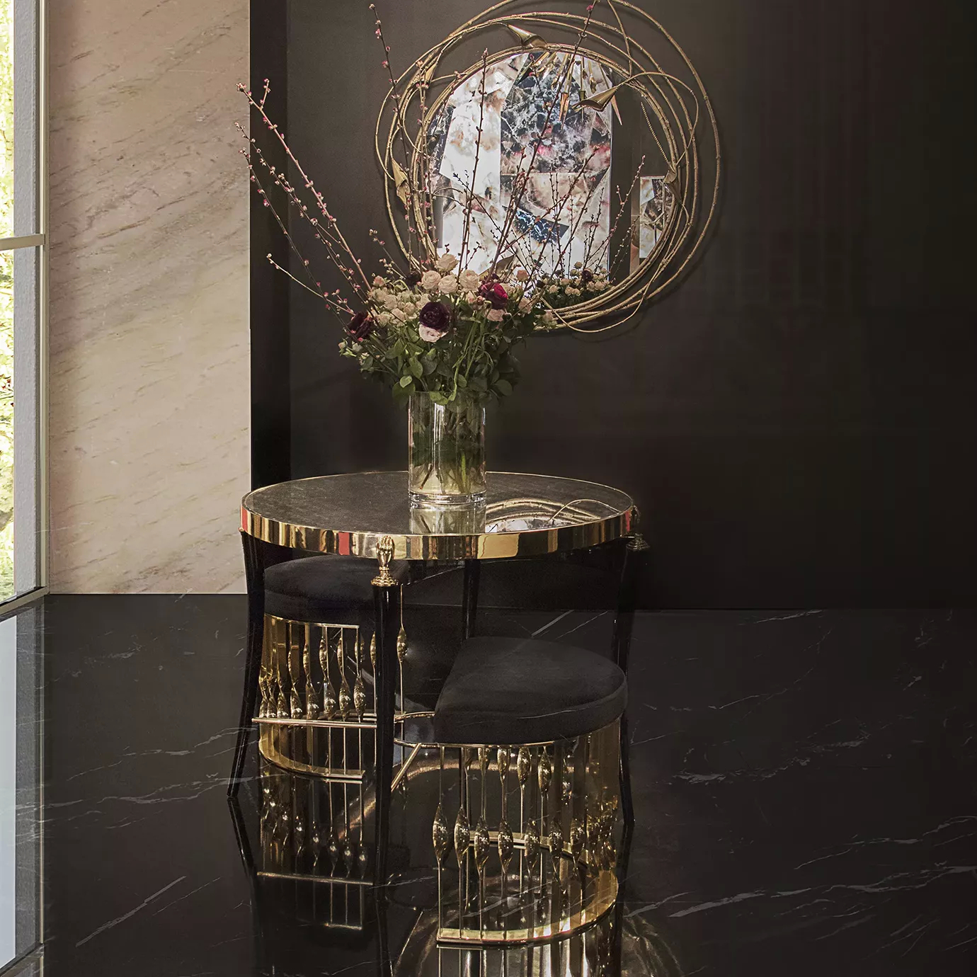 Gisele Table with a dark patterned top and golden rim, paired with two black and gold stools in a stylish room with a floral arrangement and mirror.