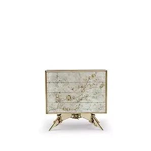 The Spellbound Aged Mirror Nightstand is adorned with a golden frame and elegant golden flower-shaped details along its four drawers.