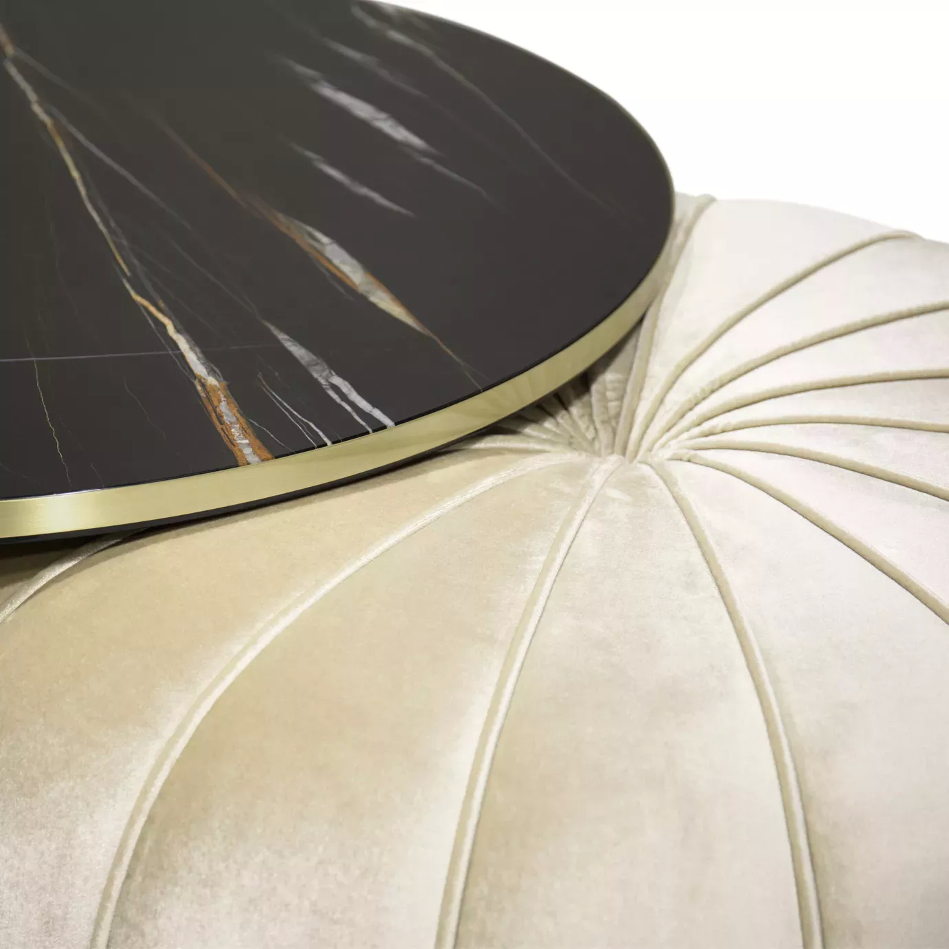 Elegant close-up of the Embrace table with Sahara Noir marble and cream velvet pouf with golden detail.