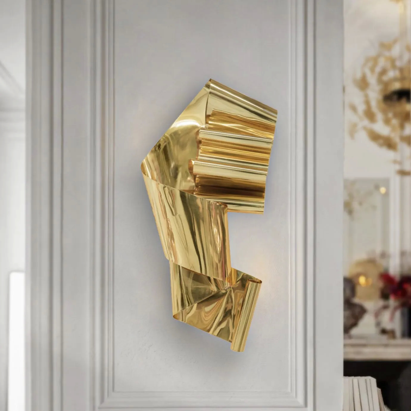 KOKET Neurotic wall sculpture in polished gold brass, featuring a fluid, abstract folded-ribbon design on a classic white architectural wall.